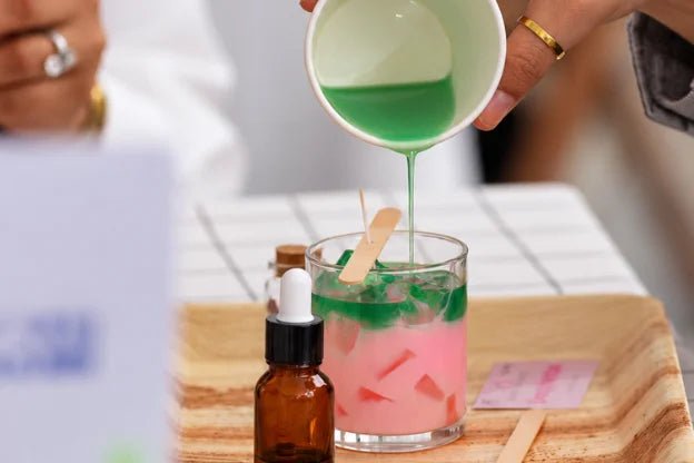 Pouring green wax over pink wax in a glass candle jar
