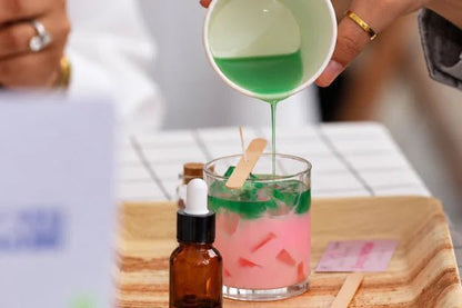Pouring green wax over pink wax in a glass candle jar